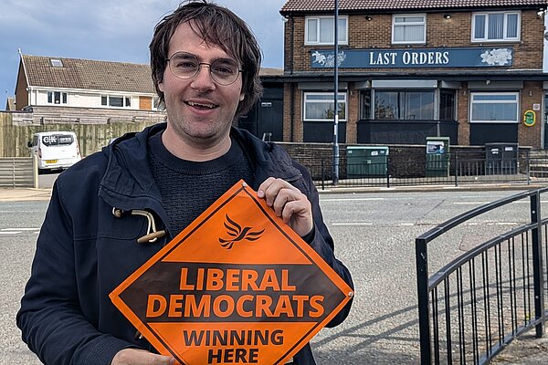 Paul Edgeworth standing holding a Liberal Democrats 'Winning Here' sign