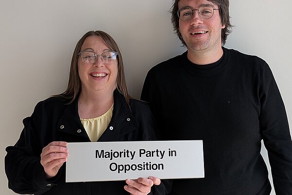 Heather Fagan and Paul Edgeworth smiling and holding a sign saying 'Majority Party in Opposition'