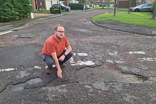 Michael Peacock crouching down and pointing at potholes on a road surface