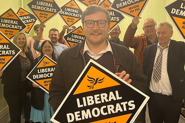 Ciaran Morrissey standing in front of supporters holding Lib Dem diamond posters